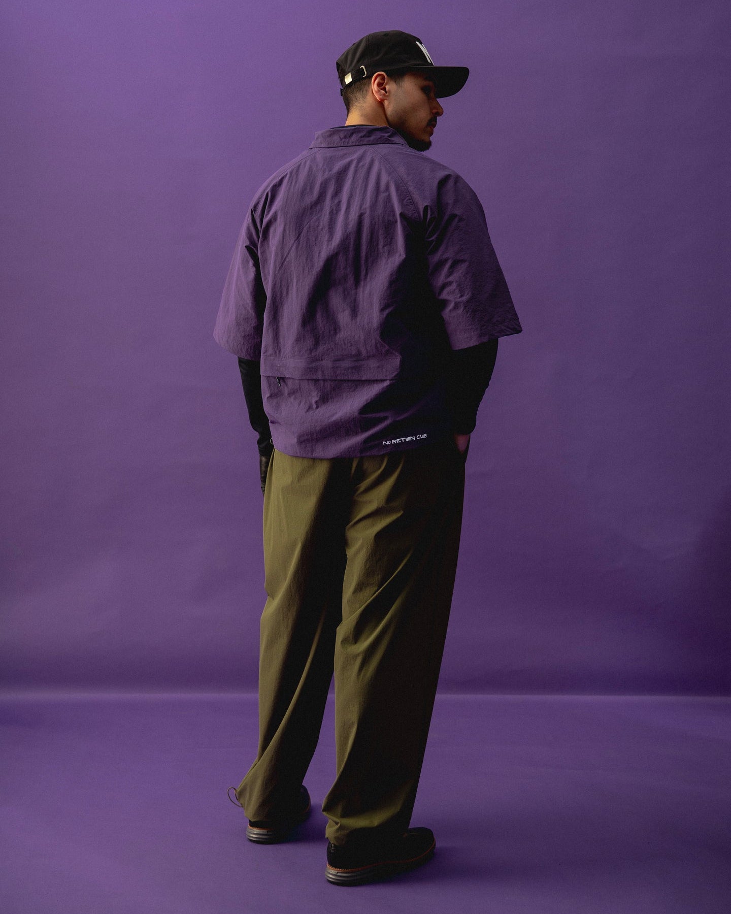 Person wearing a purple jacket and green pants against a purple background